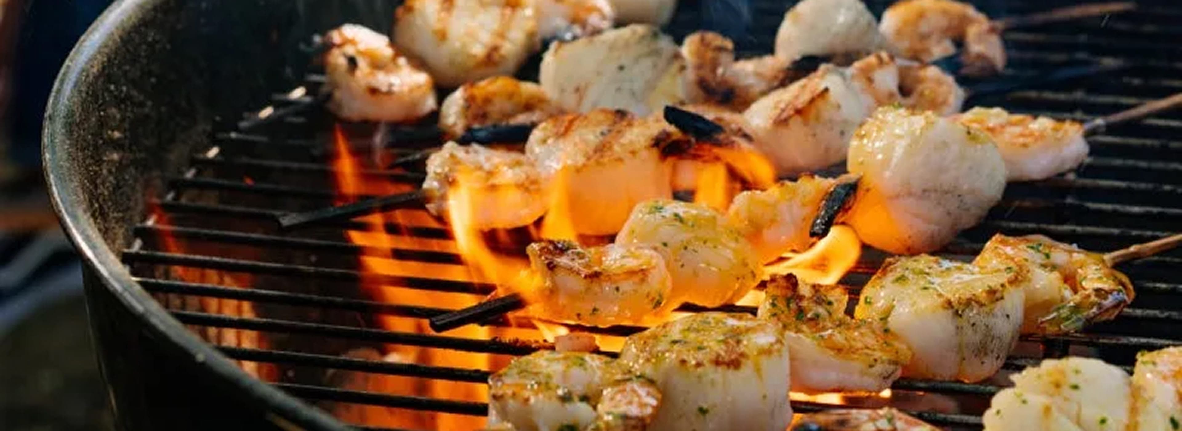 Grilled shrimp and scallop skewers cooking over open flames on a charcoal grill.